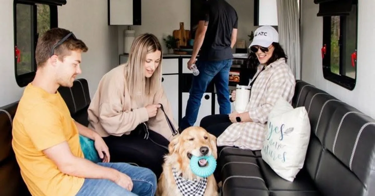 Family relaxing inside a spacious toy hauler trailer with comfortable seating, modern amenities, and a friendly golden retriever.