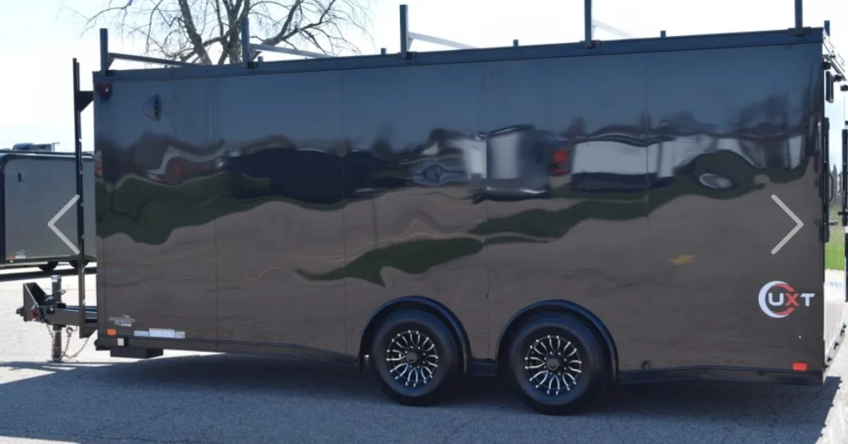 A long, black contractor trailer with all black trim and a ladder at the end to climb on top. There are two wheels.