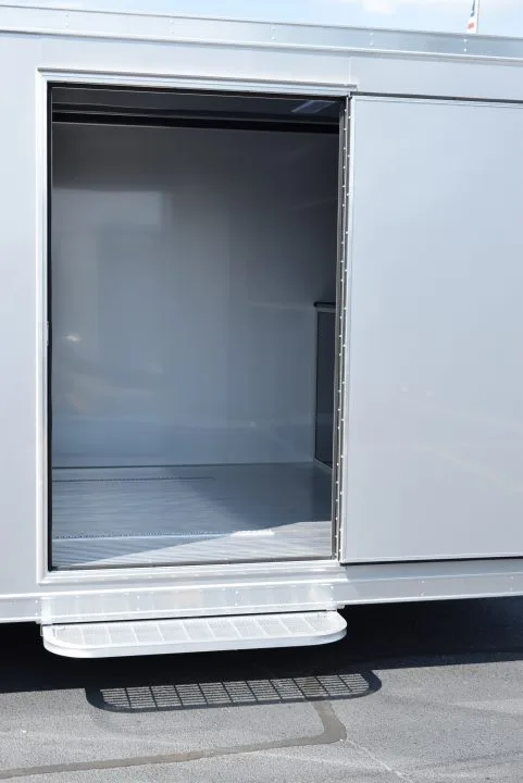 A close-up of the side door on a trailer with living quarters. The door is open and has a step outside.