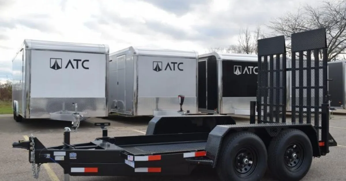 A black scissor lift trailer parked in the parking lot at the trailer store. There are two trailer haulers behind it.