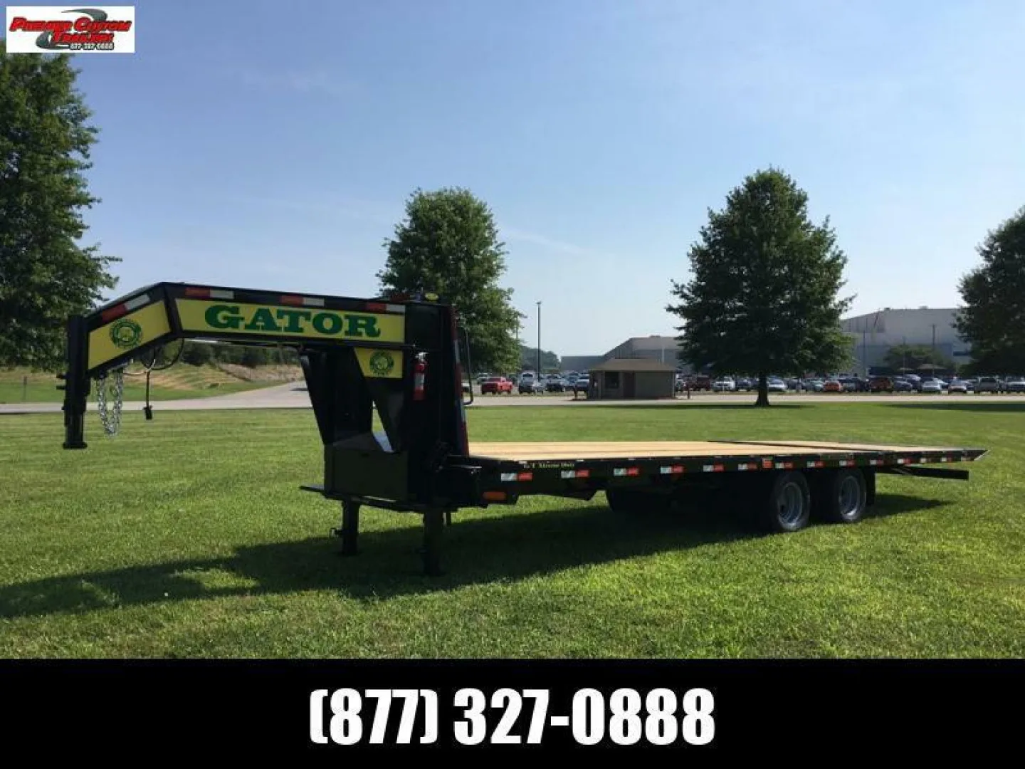 A heavy equipment trailer sits parked in the grass at the sales lot. It's sunny outside and the trailer has a black frame.